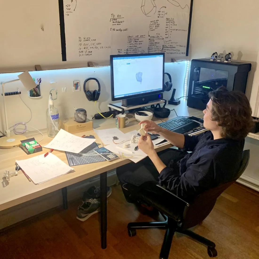 Oliver at his desk designing an OGC handle in CAD, surrounded by 3D-printed prototypes and hand sketches.